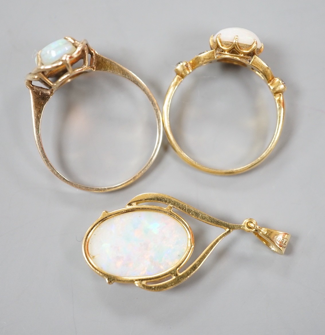 A 9k yellow metal and oval white opal set ring, size O, gross 2.1 grams, an 18ct yellow metal and oval white opal ring, with diamond chip set shoulders and a 70 and white opal set pendant, gross 5.2 grams.
